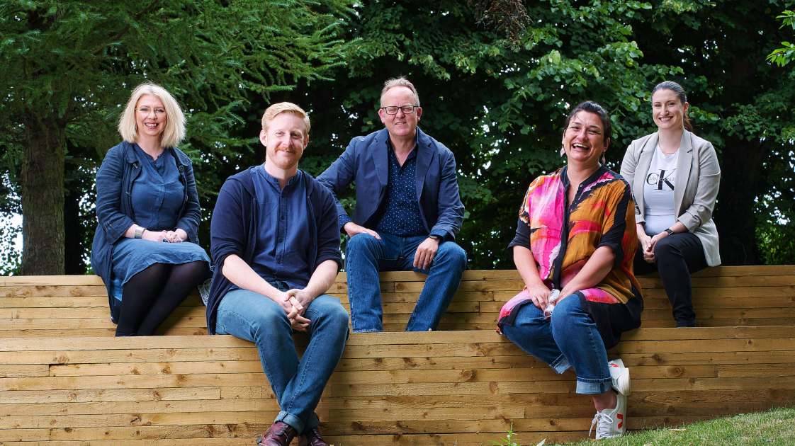Una Nic Eoin, Michael Patrick, Jimmy Fay, Emma Jordan, Natalie Murphy sitting in the outdoor amphitheatre at the Lyric Theatre