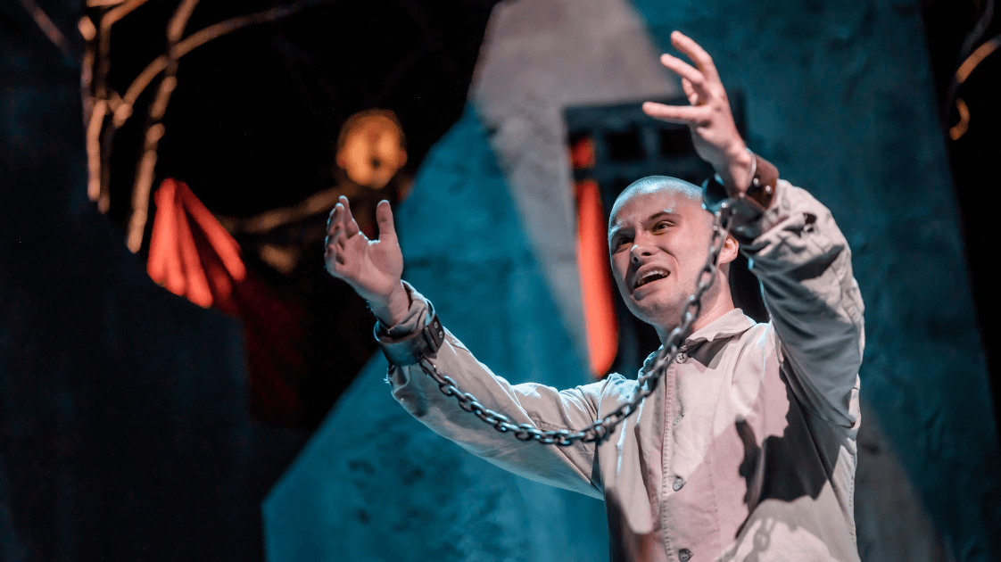 A still from Lyric Drama Studio production, Dracula featuring a man holding his arms aloft with his wrists in shackles.
