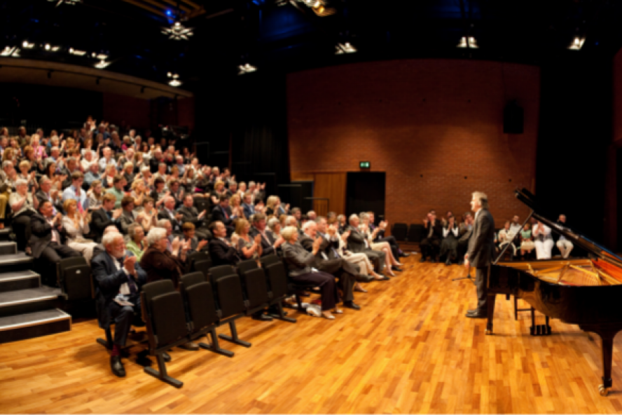 An audience applaud a performer standing on stage beside a grand piano in the Naughton Studio at the Lyric.